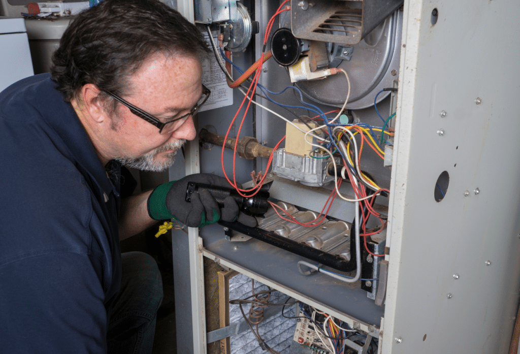 A technician wearing protective gloves inspects and repairs the internal components, wiring, and controls of an HVAC furnace.